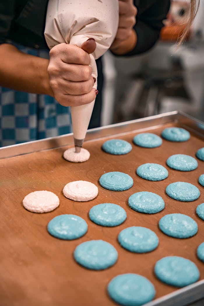 Close-up of hands piping colorful macarons on a tray, showcasing pastry art.