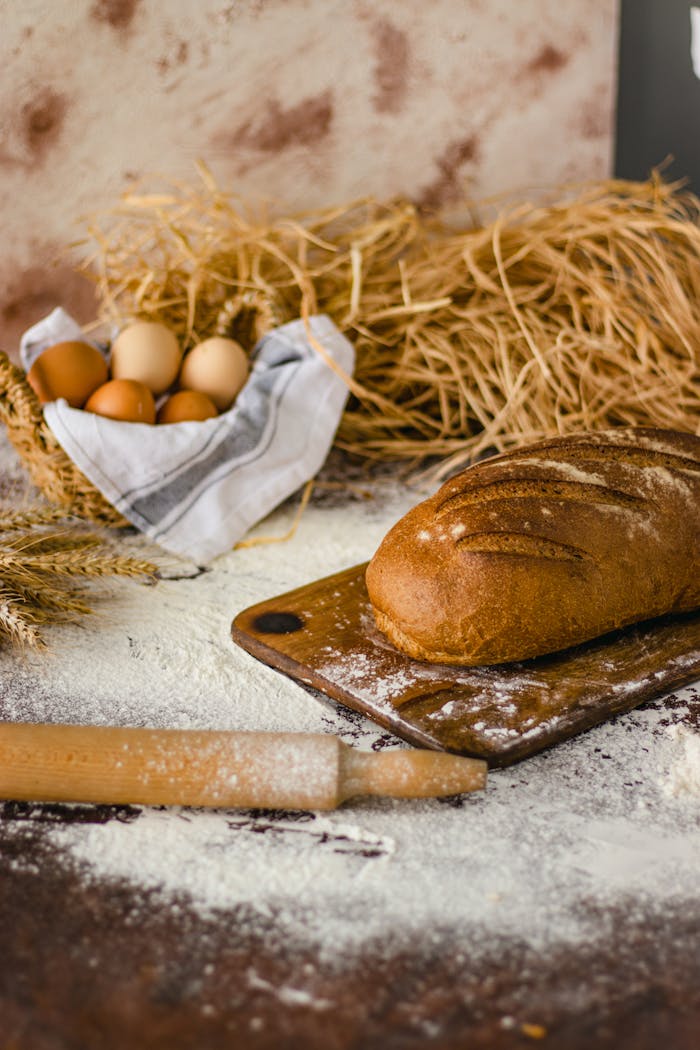 A rustic loaf of bread in a kitchen setting with eggs and wheat, ideal for baking and culinary themes.