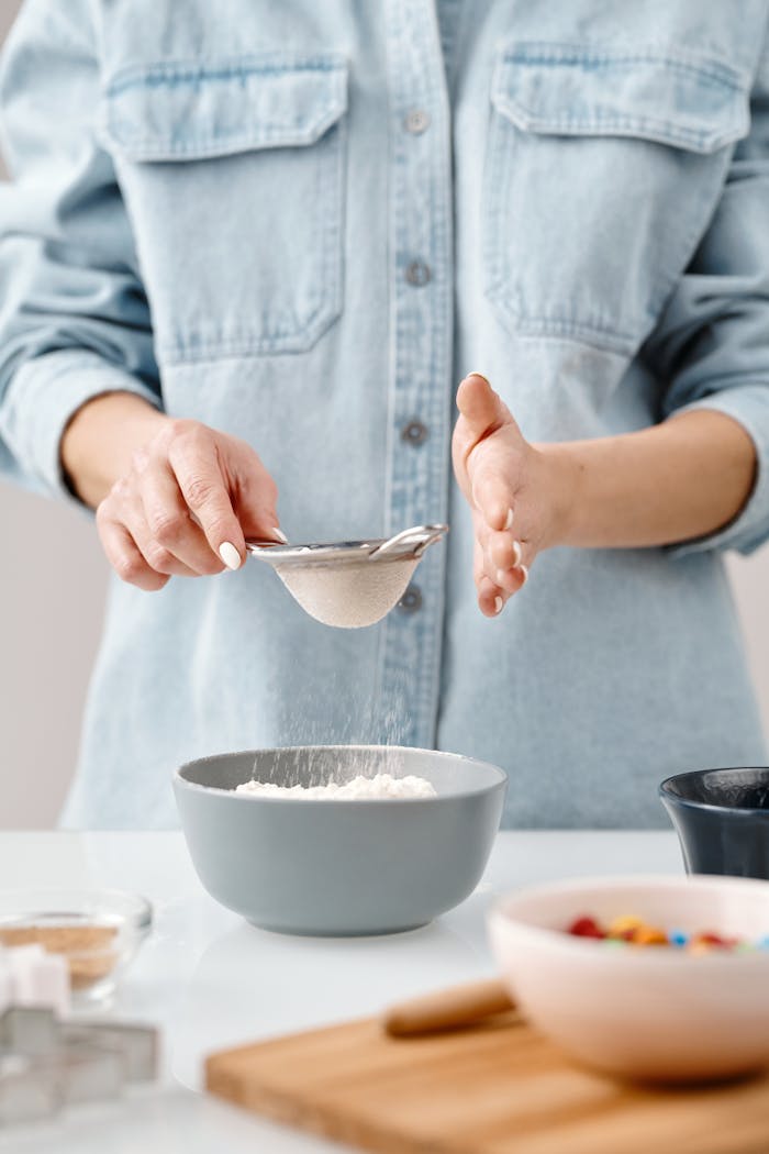 Close-up of a person sifting flour into a bowl during baking preparation.